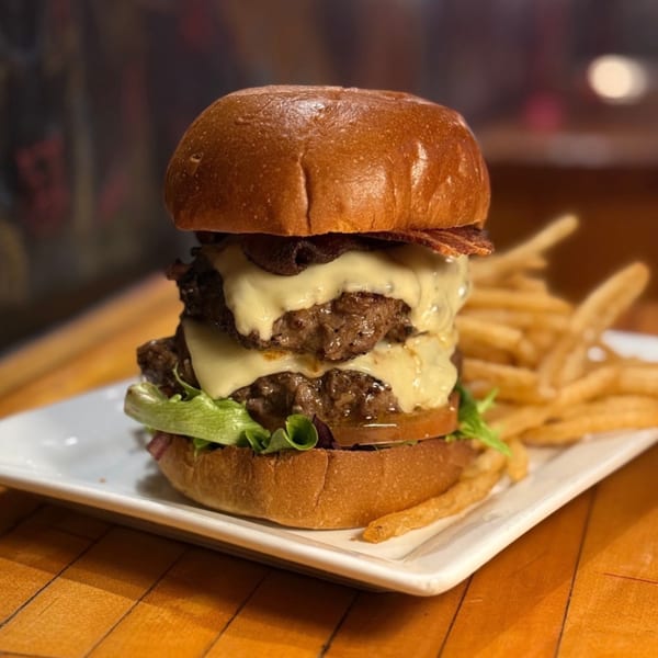 A double cheeseburger with melted cheese, bacon, lettuce, and tomato, served with fries.