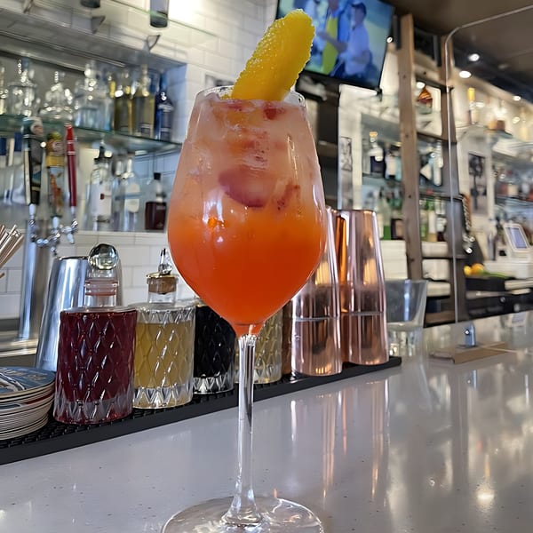 A vibrant orange cocktail with a lemon peel garnish sits on a glossy bar counter at The Surfing Pig.