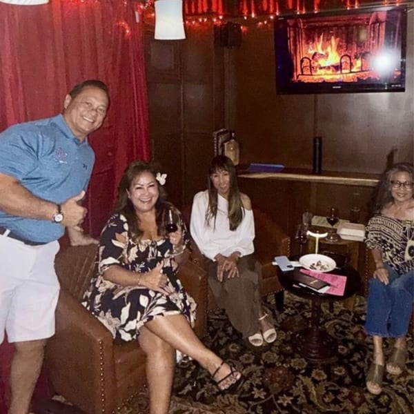 Four smiling people relaxing in a dimly lit lounge with a TV displaying a fireplace.