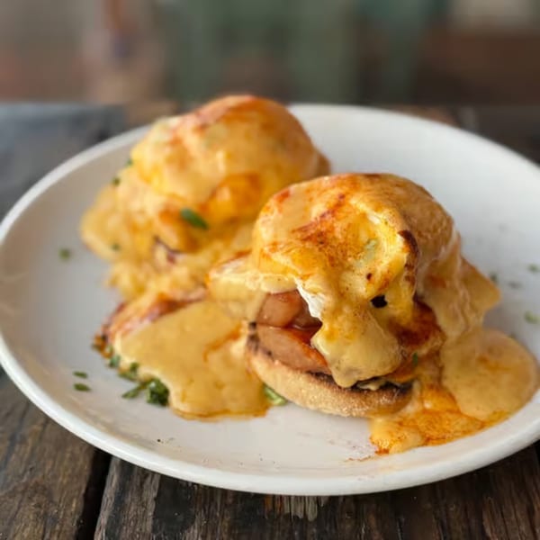Two servings of Eggs Benedict with thick hollandaise sauce and sausage on a white plate.