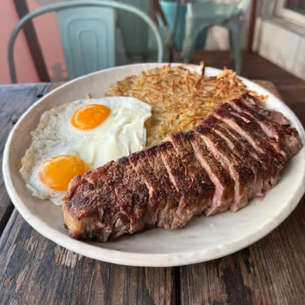 Sliced steak, two fried eggs, and hash browns on a white plate at The Surfing Pig.