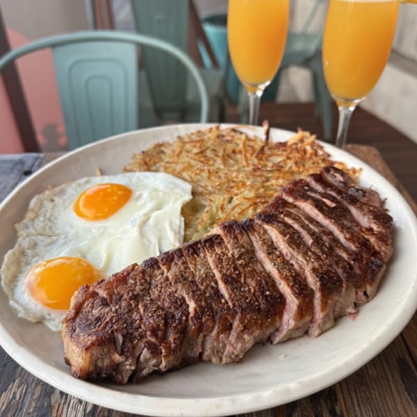 Steak and eggs with hash browns and two mimosas on a wooden table at The Surfing Pig.