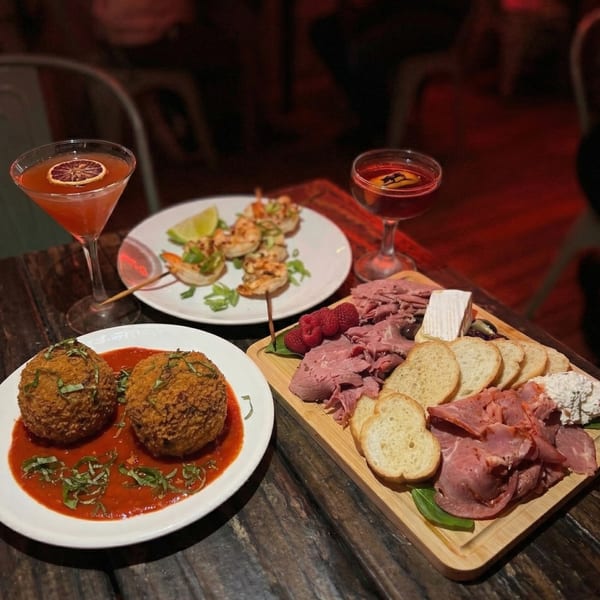 A table spread with cocktails, arancini, shrimp skewers, and a charcuterie board.