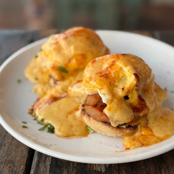 Two servings of Eggs Benedict with thick hollandaise sauce and paprika on a white plate.